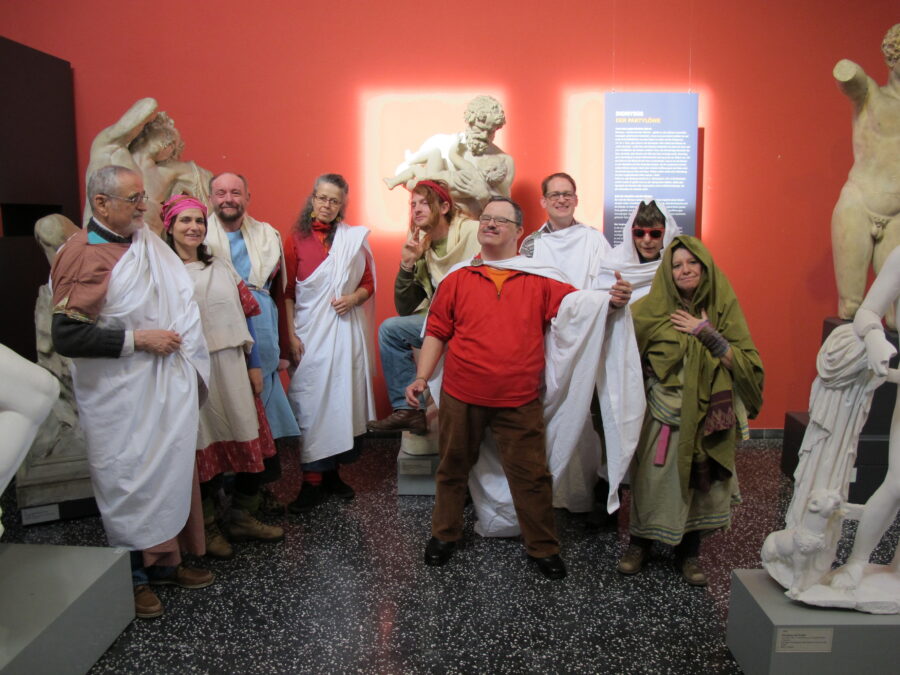 Menschen sind angezogen wie Statuen. Sie stellen Statuen nach. Im Hintergrund sind ein paar Statuen zu sehen.