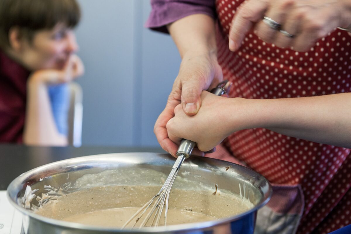 Eine Person hat einen Schwingbesen in der Hand und rührt in der Pfanne unter Anweisung die Schokocreme