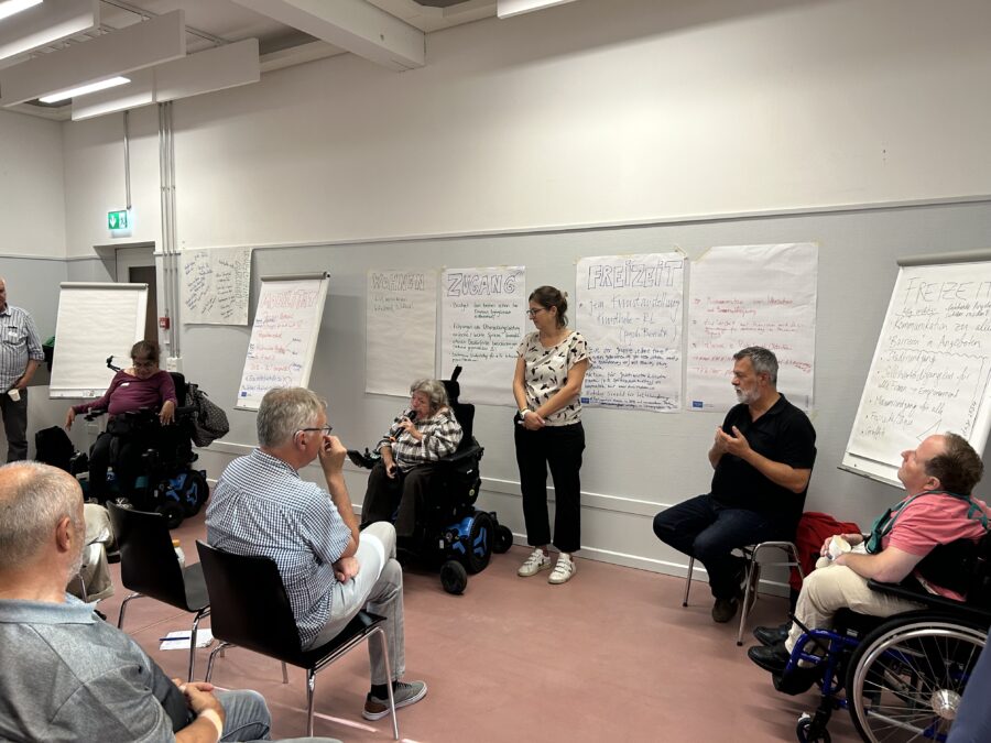 Wir sehen eine Gruppe von Leuten, die vor einer Flipchart dem Plenum die Ergebnisse präsentieren.