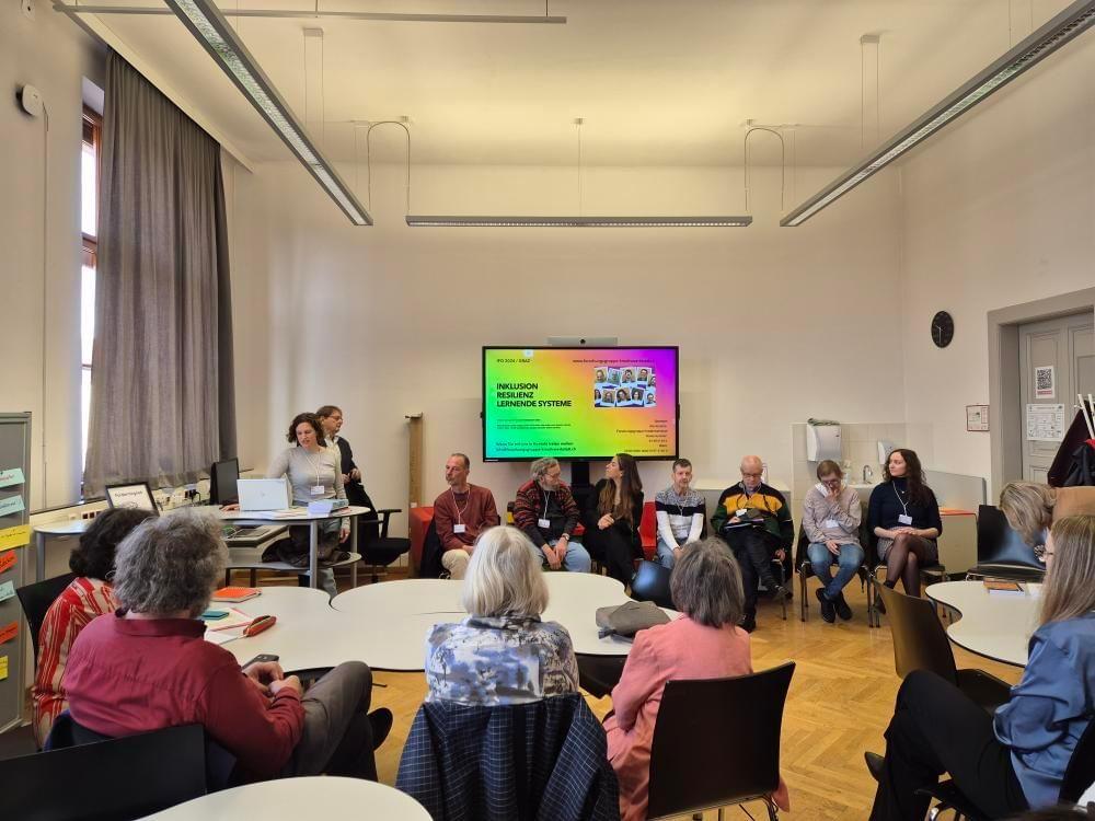 Auf dem Foto sieht man die Forschungsgruppe Kreativwerkstatt in einem Raum einen Vortrag vor Publikum halten. Sieben Mitglieder der Forschungsgruppe Kreativwerkstatt sitzen vor einem Bildschirm, zwei Mitglieder stehen davor.