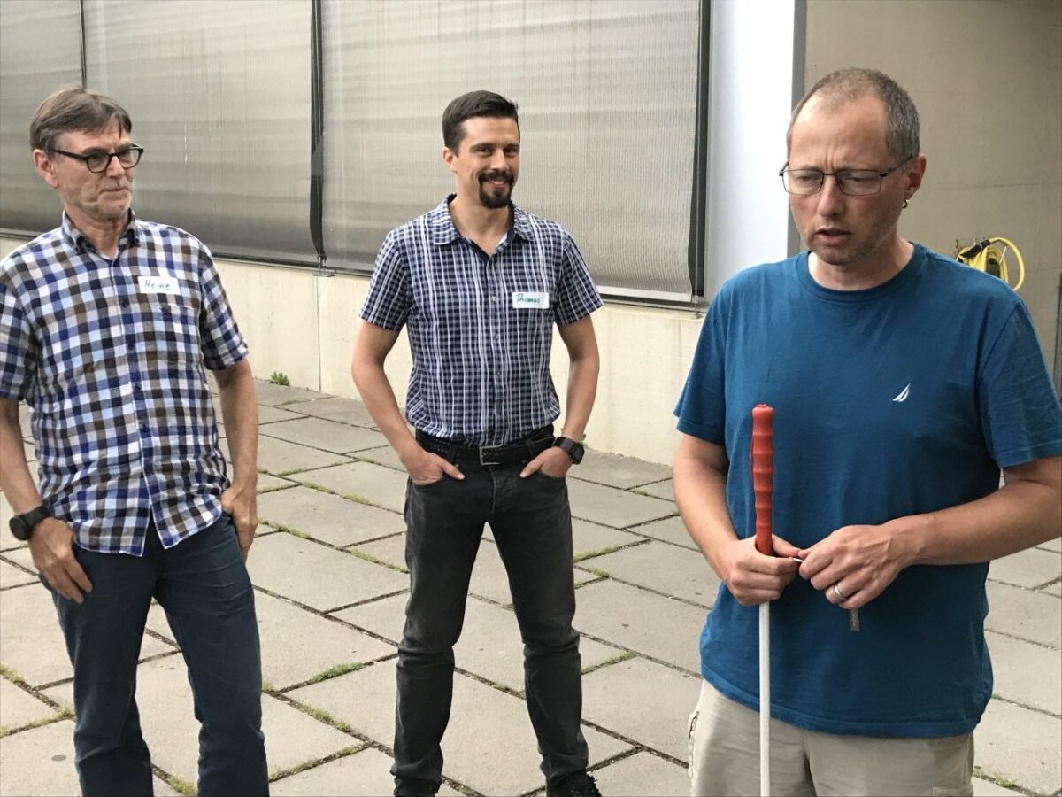 Zwei Mitarbeitende schauen und hören einer Person am Blindenstock zu.