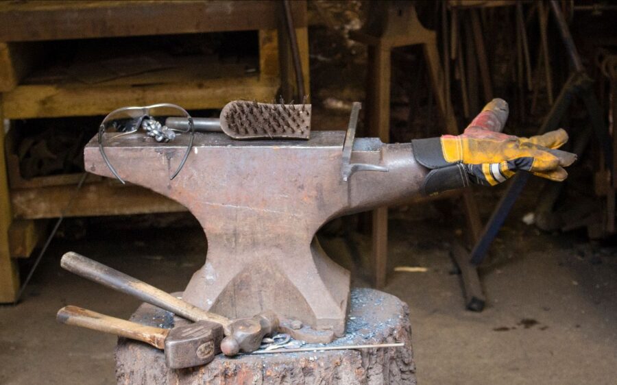 Verschiedene Werkzeuge und ein gelber Handschuh liegen auf einem Holzstumpf.