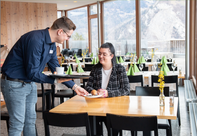 Ein Mann serviert einer Frau im Restaurant einen Kaffee und Kuchen.