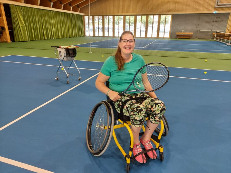 Frau in einem Tennisrollstuhl in einer Innenhalle.