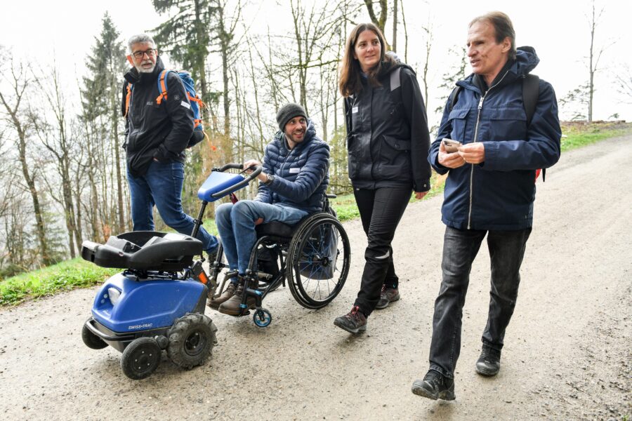 Vier Personen sind am Wandern. Eine Person sitzt im Rollstuhl.