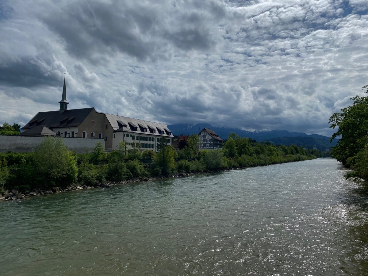 Blick über die Reuss zum Pausenort Rathausen mit Klosterteil und altem Fachwerkhaus. Im Hintergrund der Pilatus in Wolken.