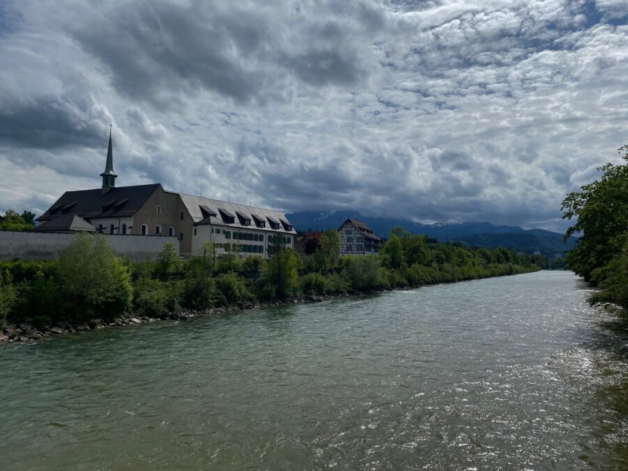 Blick über die Reuss zum Pausenort Rathausen mit Klosterteil und altem Fachwerkhaus. Im Hintergrund der Pilatus in Wolken.