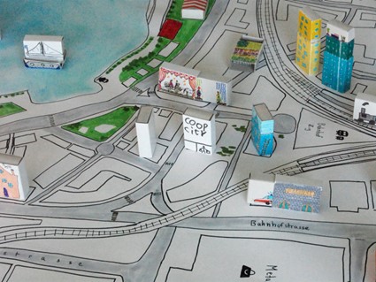 Gemeinsam Stadträume und Stadtträume entwerfen: Eine künstlerische Darstellung der Stadt Zug, gezeichnet auf Papier. Einige Gebäude sind mit bemalten Streichholzschachteln dargestellt.