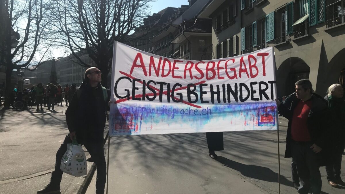 Schriftzug: 'Andersbegabt, geistig Behindert' - 'geistig' durchgestrichen mit einem roten X. Unten steht die E-Mail-Adresse: gruppe-mitsprache.ch