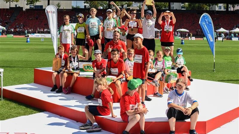 Mehrere Kinder sitzen auf eine Tribüne und halten ihre Pokale in den Händen.