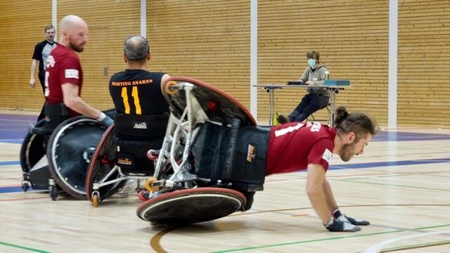 Menschen in einem Rollstuhl sind in einer Sporthalle und spielen Rollstuhl-Rugby.