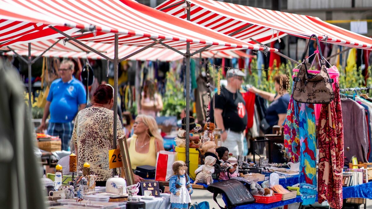 An Marktständen werden bunte Kleider, Spielzeuge, Schmuck und Geschirr zum Verkauf angeboten.