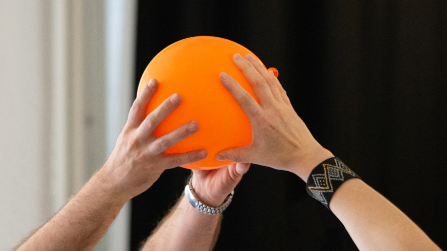 Auf dem Bild ist ein Ball zu sehen, den verschiedene Personen gemeinsam in der Luft halten und weitergeben, ohne dass er herunterfällt. So arbeiten sie gemeinsam und doch jede auf ihre Weise daran, dass dieses Ziel gelingen kann.
